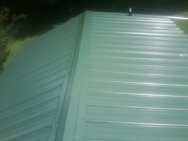 New green metal panels meeting at the ridge of a roof — Flat Roof Repair work by our crew in Fredonia