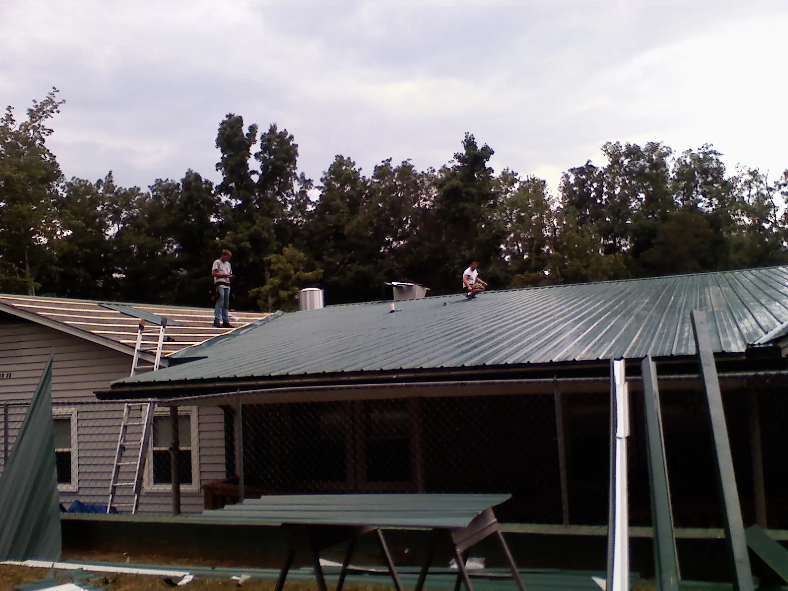 Two roofers installing green metal panels above a covered porch in Fredonia